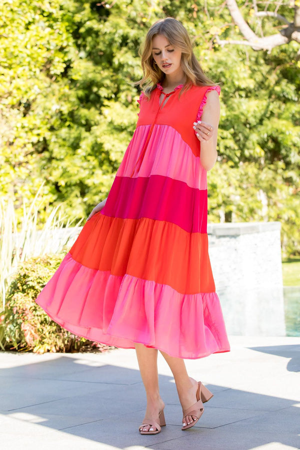 Woman wearing pink and red midi length tiered dress with v-neck and tie on neck 